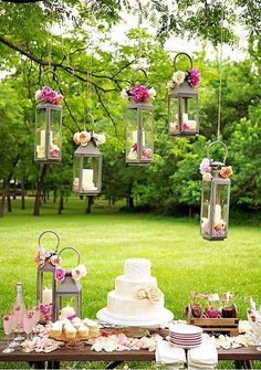 a table topped with lots of cakes and cupcakes next to a lush green field