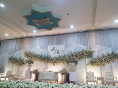 a decorated stage with white flowers and greenery on the wall, surrounded by chairs