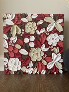 a red and white flowered painting on a wooden floor next to a black vase