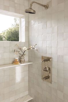 a white tiled bathroom with a window and shower head