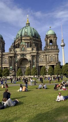 many people are sitting on the grass in front of a large building with green domes