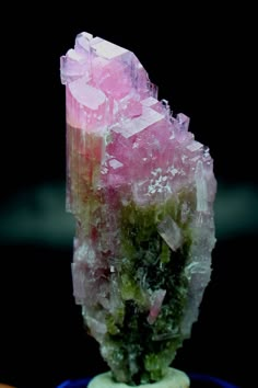 a large piece of pink and green crystals on top of a blue object with other items in the background