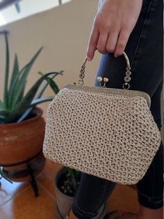 a woman is holding a crocheted purse in front of a potted plant