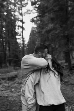 black and white photograph of a couple embracing in the woods with trees in the background