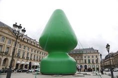 an inflatable green object sitting on top of a cement ground next to buildings