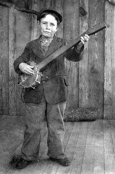 an old black and white photo of a young boy holding a guitar in his right hand