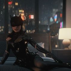 a woman dressed in catwoman costume sitting on a bed with city lights behind her