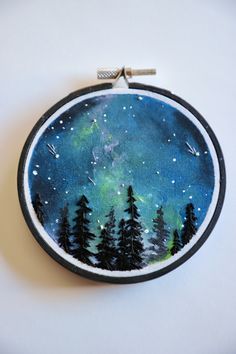 a hand embroidered ornament depicting the night sky with stars and trees on it