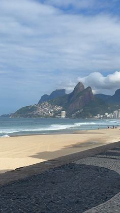 people are walking on the beach with mountains in the background