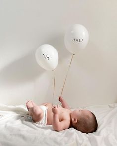 a baby laying on its back holding two balloons with the words half written on them