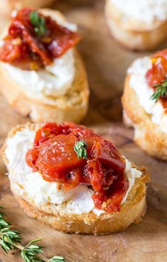 small crostini with tomato sauce and cheese on a wooden cutting board next to fresh herbs