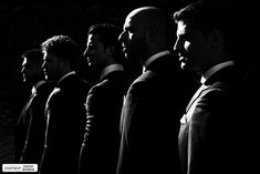 a group of men standing next to each other wearing suits and ties in black and white