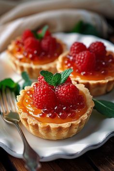 two small tarts with raspberries and mint on a plate next to a fork