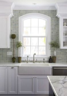 a kitchen with marble counter tops and white cabinets, an arched window over the sink