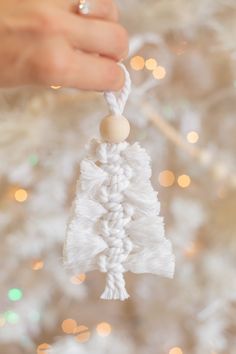 a hand holding a white christmas ornament in front of a tree