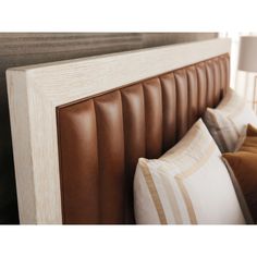 the headboard of a bed with brown leather and white pillows