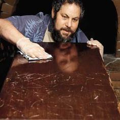 a man leaning over a wooden table with gloves on his hands and looking at the camera