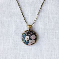 Inspired by Liberty Art Fabric, I developed my collection of vintage-style jewellery. The vibrant floral motifs of Liberty fabric are truly celebrated and showcased in this collection. A great gift for nature-lovers that will never go out of fashion. This necklace features white flowers in the dark background which has an oriental painting feeling. It has an antique bronze alloy pendant tray and an oval pendant. The long brass chain has a lobster clasp and a tiny bee beside it. Pendant 2.8 x 2.8 Vintage Necklaces With Flower Charm Round Pendant, Vintage Necklace With Flower Charm Round Pendant, Vintage Necklace With Round Pendant And Flower Charm, Vintage Multicolor Necklace With Adjustable Chain, Vintage Flower Pendant Necklace With Adjustable Chain, Vintage Necklace With Flower Pendant And Adjustable Chain, Vintage Flower Charm Pendant Jewelry, Vintage Jewelry With Flower Charm And Pendant, Vintage Pendant Necklace With Flower Charm