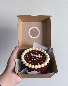 a person holding up a box with a cake in it that says twenty two on the inside