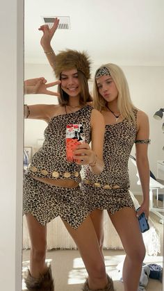 two women dressed in animal print outfits are posing for the camera while one holds up a cell phone