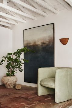 a living room with a chair and a plant in the corner next to a painting on the wall