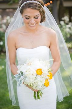 a woman in a wedding dress holding a white and yellow bouquet with orange flowers on it