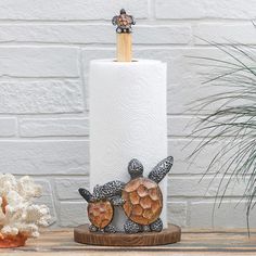 two turtle figurines sitting on top of a toilet paper holder next to a potted plant