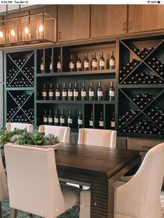 a dining room table surrounded by white chairs and bottles of wine on the wall behind it