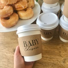 a person holding up a cup of coffee next to doughnuts