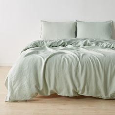 an unmade bed with two pillows on top of it and a light green comforter