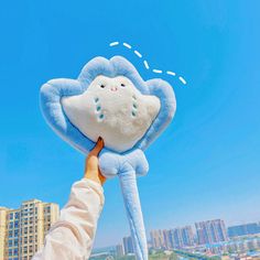 a person holding up a blue and white stuffed animal in front of a cityscape