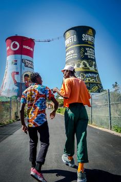 two men are walking down the road in front of a tower