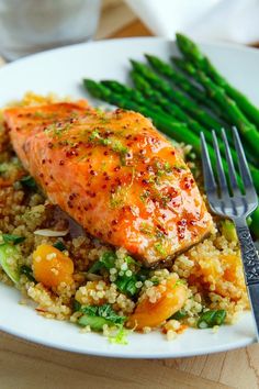 a white plate topped with salmon and rice next to asparagus