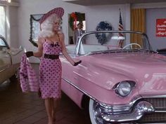 a woman standing next to a pink car