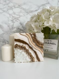 a marble block next to a candle and some flowers on a white table with a chandelier in the background