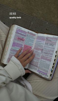 a person sitting down reading a book with their hands on the open pages and writing