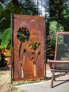 a rusted metal sign with flowers on it next to a wooden chair and tree