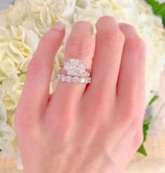 a woman's hand with two wedding rings on it and flowers in the background