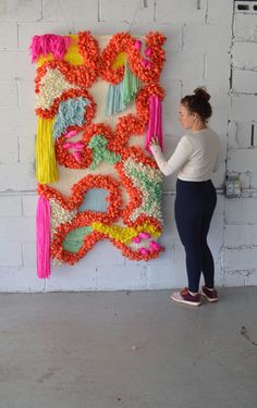 a woman is standing in front of a wall hanging with flowers and tassels