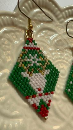 a pair of green and white beaded christmas tree earrings sitting on top of a plate