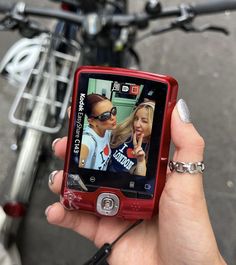 a person holding up a red cell phone with two girls on it's screen