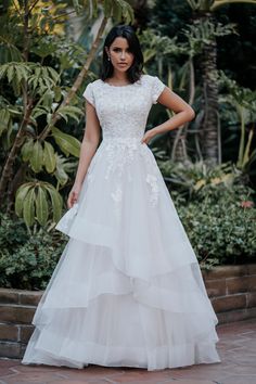 a woman in a white wedding dress standing on a brick walkway with her hands on her hips