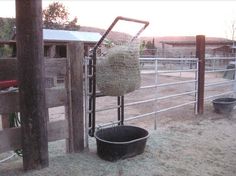 an animal pen with hay in it and a bucket on the ground next to it