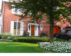 a black car parked in front of a red brick house with white flowers on the lawn