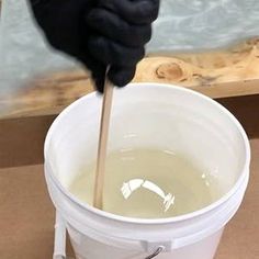 a person in black gloves holding a wooden stick over a white bucket filled with water