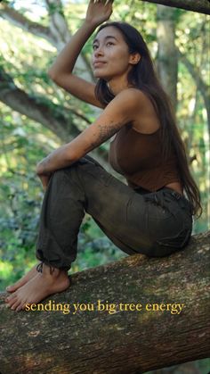 a woman sitting on top of a tree branch in the woods with her arms behind her head