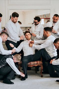 a group of men standing around each other tying their ties in a room with white walls