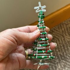 a hand holding a small christmas tree made out of beaded wire and beads,