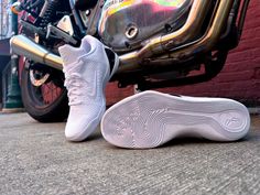 a pair of white sneakers sitting on the ground next to a parked motorcycle in front of a red brick wall