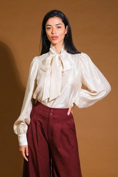 A woven top featuring front bow tie and long blouson sleeve with cuff Details: Self : 34% Tencel 34% Nylon 32% Polyester Size & Fit - Model is 5`8" And Wearing Size Small- Measurements Taken From Size Small- Approx. Length: 23" Fall Puff Sleeve Blouse With Bow Detail, Fall Puff Sleeve Blouse With Bow, Classic Long Sleeve Blouse With Bow, Long Sleeve Blouse With Bow For Work, Chic Long Sleeve Tops With Bow, Fall Tie Neck Blouse With Bow, Fall Tie Neck Top With Bow Detail, Fall Tie Neck Top With Bow, Long Sleeve Tops With Bow For Work